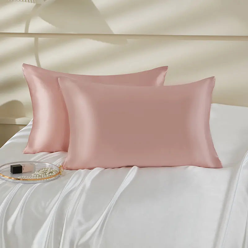 Coppia di federe in seta rosa cipria su letto bianco, accessorio elegante per la camera da letto.